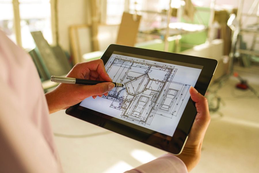 A person using a stylus on a tablet displaying architectural blueprints, set in a construction environment with building materials and scaffolding in the background.