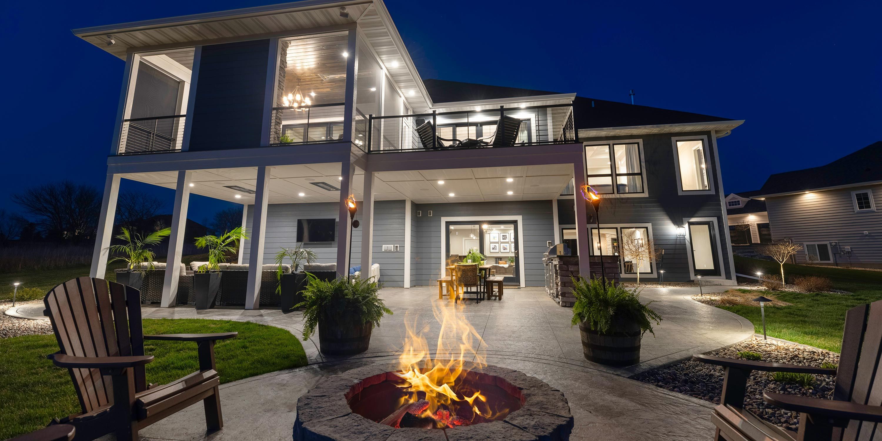 Outdoor patio with a fire pit, seating, and a two-story house at night